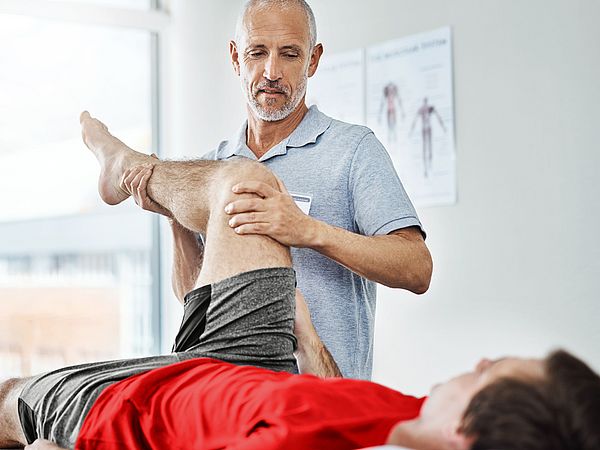 Ein Arzt untersucht das Kniegelenk eines männlichen Patienten